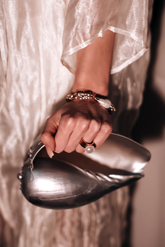 A woman's hand with a pearl ring holding an interesting handbag in the shape of a silver seashell