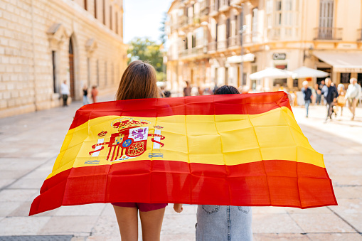 Rear-view of two beautiful female friends waving a Spanish flag on the street in Málaga in Spain.