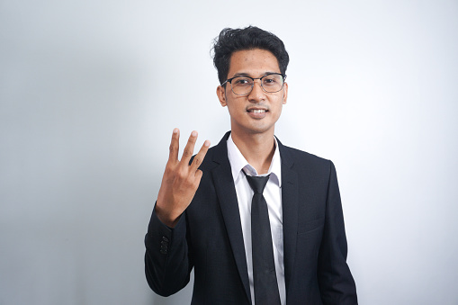 Young handsome Asian man wearing suit showing and pointing up with fingers number three while smiling confident and happy.