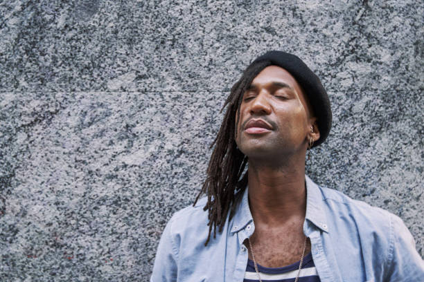 istock handsome African-American man in braids with stylish beret looking away while standing against grey wall and eyes closed 2134846395
