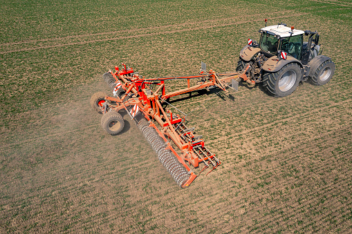Agricultural tractor harrowing and plowing field in spring, aerial view.