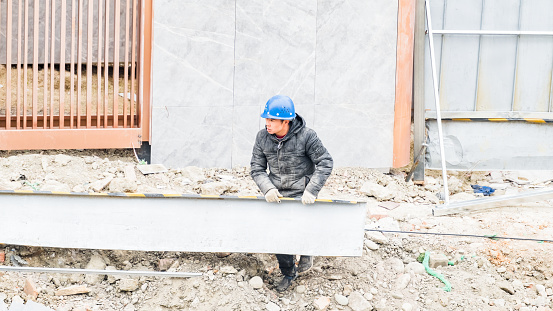 On February 22, 2024, on a cloudy day, at a construction site in Shuangliu District, Chengdu City, Sichuan Province, a middle-aged male worker was carrying and sorting out excess iron sheets and iron bars.
