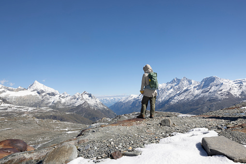 Zermatt, Switzerland  A hiker stands high up at Trockener Steg, taking in the expansive view of the snow-capped Swiss Alps, a testament to the serene and awe-inspiring mountain vistas.