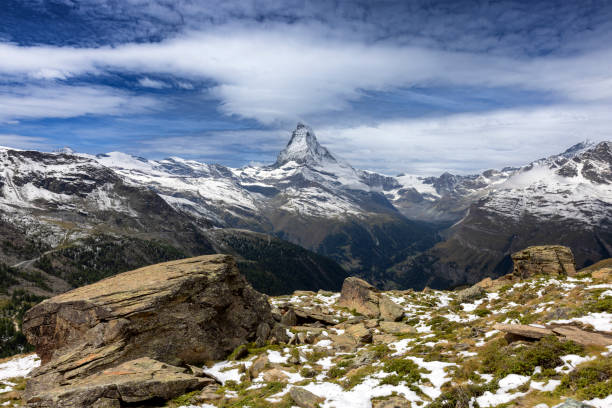 Caption: Zermatt, Switzerland - August 31, 2023: A stunning view of the iconic Matterhorn mountain, rising majestically above the surrounding Alpine landscape, with snow-dusted peaks under a dramatic sky.