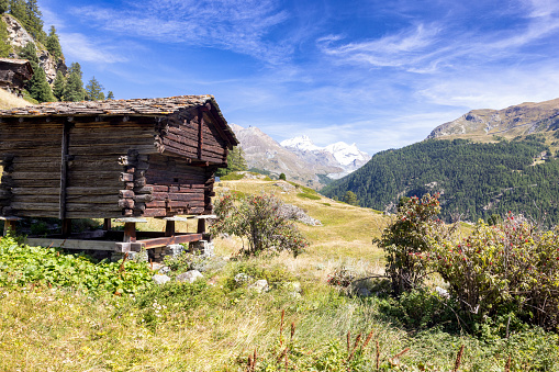 A traditional wooden Swiss house, perched on stones against a backdrop of Zermatt's picturesque landscape, offers a glimpse into the harmonious blend of culture and nature in the Swiss Alps
