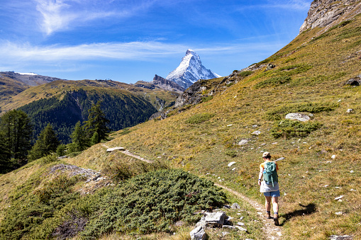 A hiker follows a trail in the Swiss Alps, with the iconic Matterhorn beckoning in the distance, a perfect blend of human endeavor and natural splendor