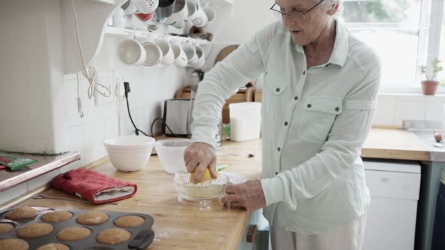 Senior woman squeezing lemon juice for a muffin recipe in her kitchen