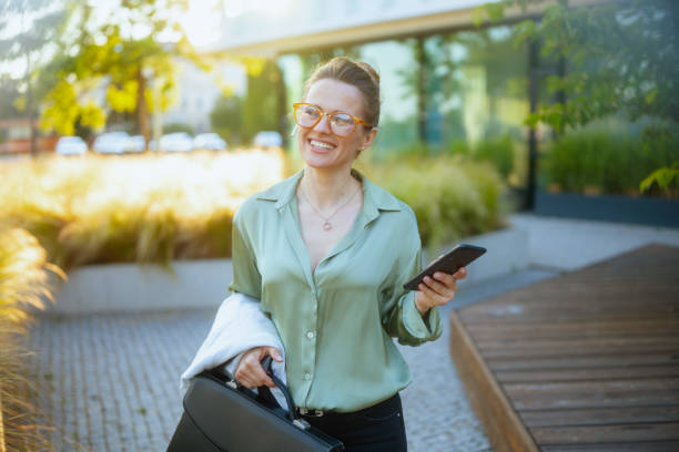 istock female worker in green blouse and eyeglasses using smartphone 2134900979