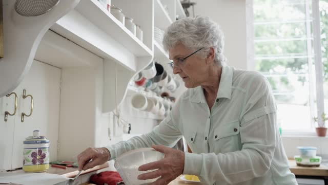 Senior woman drizzling lemon juice over muffins at her kitchen counter