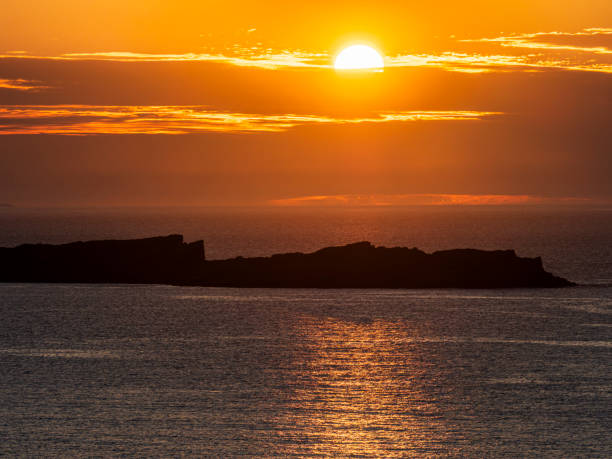 Setting sun over ocean with distant island near Dunluce Road, Bushmills, Northern Ireland, United Kingdom.