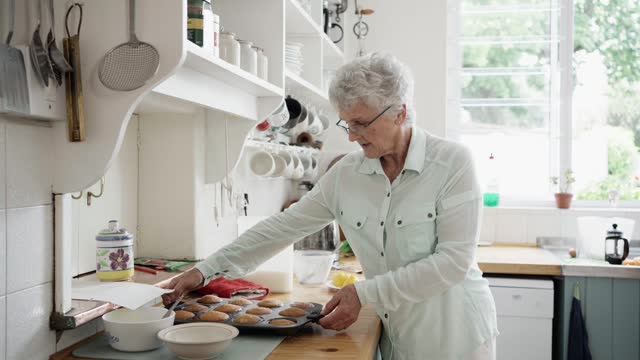 Smiling senior woman showing off a tray of fresh baked muffins in her kitchen