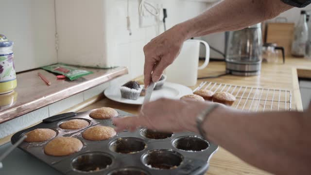 Senior woman taking freshly baked muffins out of a tray in her kitchen