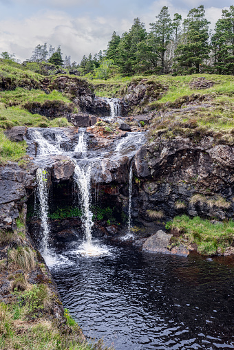 The serene waters of the Fairy Pools cascade over basalt rocks, framed by the verdant landscape of the Isle of Skye, a tranquil oasis of natural beauty