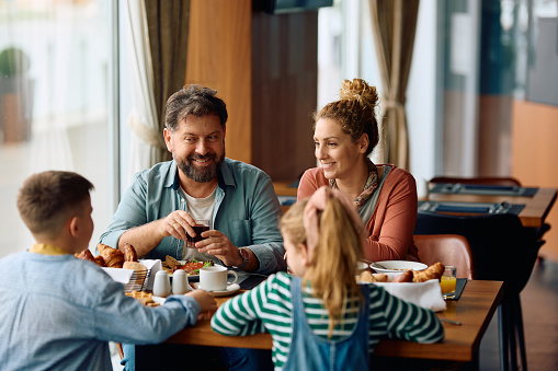 Happy parents enjoying in breakfast time with their kids in a hotel.
