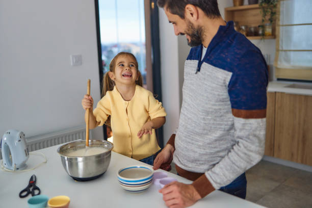 istock Young girl stands at the kitchen table making cakes with her father 2134936506