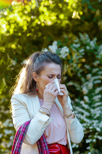 modern woman in pink dress and white jacket in the city with napkin and red bag has an allergy attack.