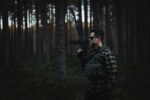 Male private military man with a modern assault rifle and body armor in the twilight forest. High quality photo