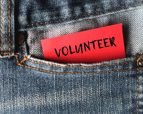 Note in jeans pocket with text VOLUNTEER, a person who does something or helping others willingly without being forced or paid to do