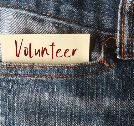 Note in jeans pocket with text VOLUNTEER, a person who does something or helping others willingly without being forced or paid to do