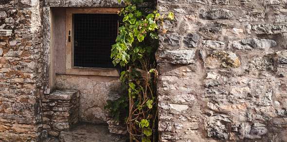 An old part of the building from the side of the yard, built from stones of different sizes; there is a niche with a closed and locked window.