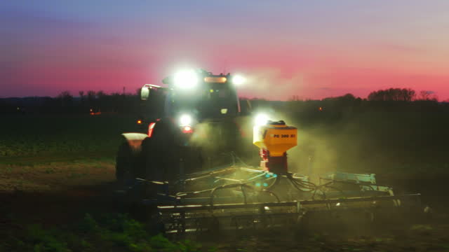 Tractor with Glowing Headlights Plowing Agricultural Land at Night