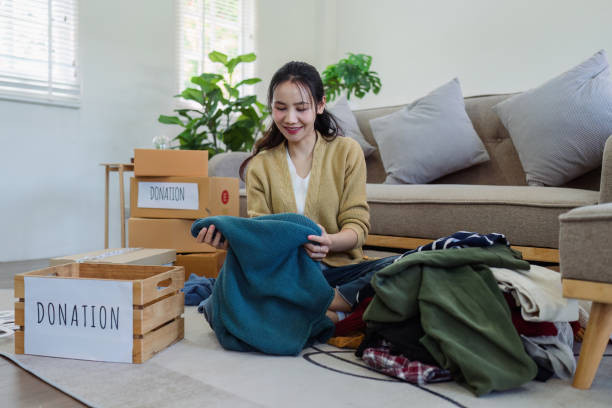 istock Asian young woman packing clothes at home, putting on stuff into donate box with second hand clothes. Help poor people. Donation concept 2135010720