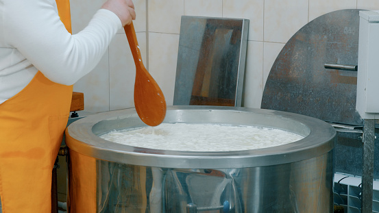 Stirring raw materials for cheese with a wooden spoon