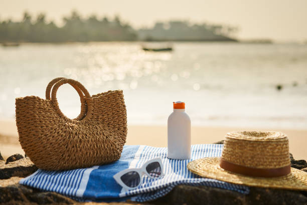 istock Beach scene with sunscreen bottle, straw hat on blue towel. Protective sunblock essential for tropical climate. UV protection gear, sunglass on sunny ocean shore. Holiday, skin care, leisure concept. 2135051152