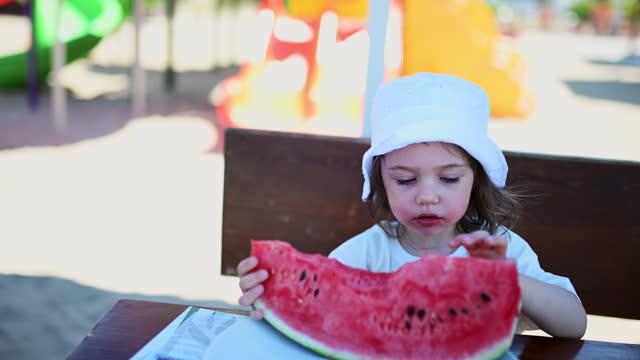 Toddler girl eating watermelon fruit at bar.