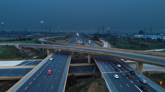 Drone flight over freeway as cars move swiftly, dark storm clouds gather ominously above, signaling an impending storm. Freeway under by nature's fury. Freeway view captures impending storm.