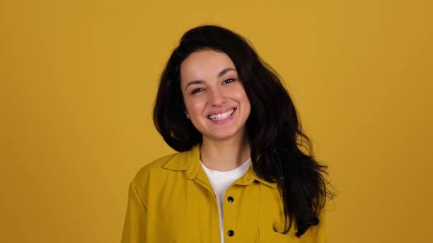 istock Happy young lady posing in studio while throwing up an orange and showing it at camera. Isolated on yellow background. Healthy nutrition concept. Real time 2135055472