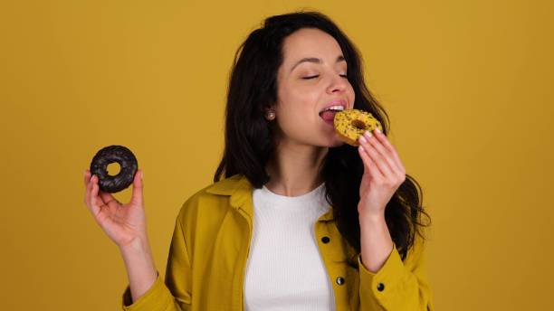 istock Smiling pretty lady choosing between two donuts and biting one, posing in studio, isolated on yellow background. Real time 2135055473