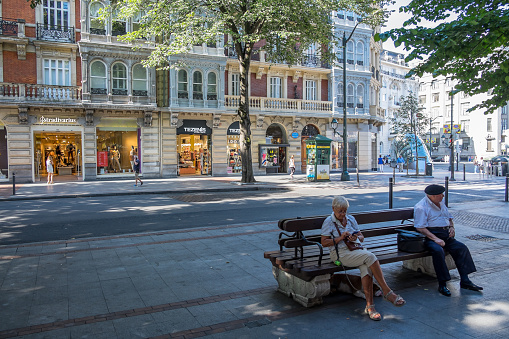 Vizcaya, Basque Country, Spain - August 11, 2018: Older people sitting on a bench in the Gran Via of Don Diego Lopez de Haro, in the urban center of the city of Bilbao