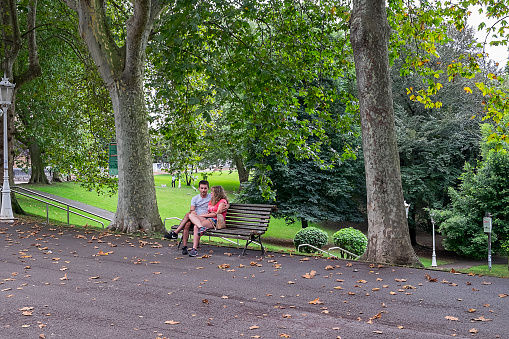 Vizcaya, Basque Country, Spain - August 01, 2018: Urban scene with a young couple sitting on a bench in the Dona Casilda park in Bilbao