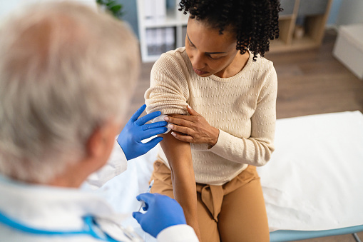 Senior Caucasian male doctor, giving a flu vaccine to a female patient African-American ethnicity, during an annual medical check-up