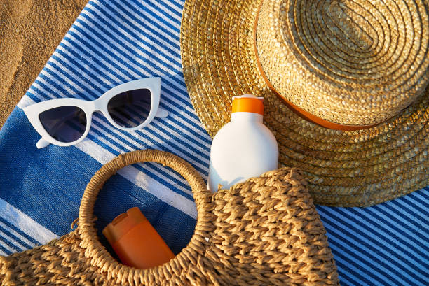 istock Beach scene with straw, white sunglasses, sunscreen in wicker bag on blue towel. Summer essentials for sun protection on sandy shore by ocean. Relaxing day at beach necessary sunbathing. 2135103746