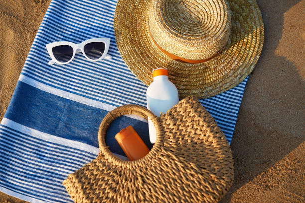 istock Sunbathing accessories on sandy beach, straw hat beside sunglasses, sunblock lotion in bag for skin protection, summer seaside holiday essentials on striped towel, outdoor UV care on sunny day. 2135109089