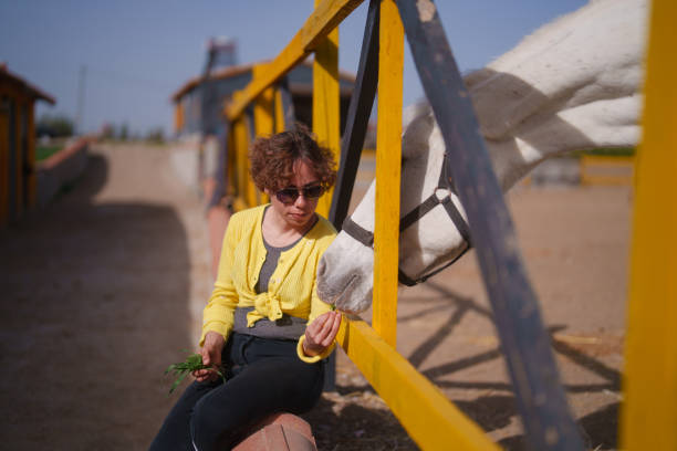 Woman sitting next to ranch and horse is putting her head off woman's shoulder.