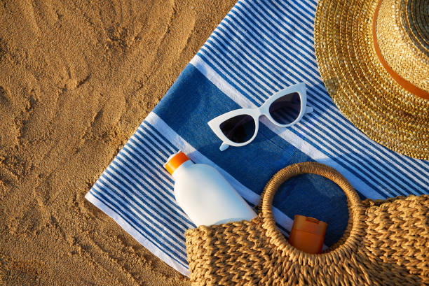 istock Summer beach essentials laid on sand for sun protection. Straw hat, white sunglasses, sunscreen bottle, and woven bag ready for day by sea. Holiday accessories for UV defense on sunny ocean shore. 2135115672