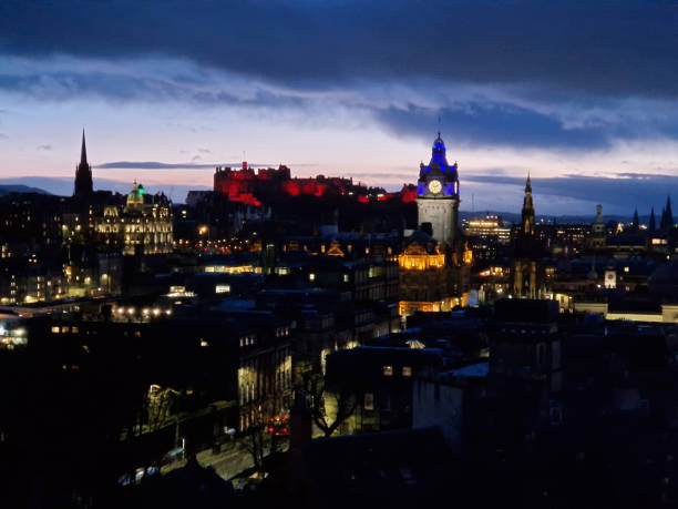 Vibrant night scene of Edinburgh's International Book Festival featuring colorful tents, warm lighting, and historic stone buildings. People mingle outdoors among benches and book stalls under strings of lights.