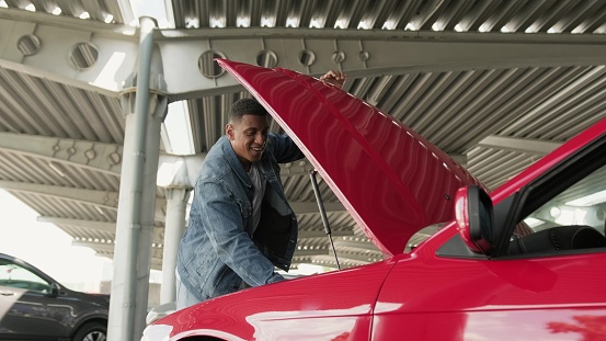 Smiling African American man repairing his car while opening the hood. Service car concept. .
