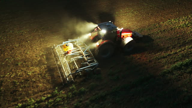 AERIAL Drone Shot of Illuminated Tractor Plowing Field for Sowing at Night in Village