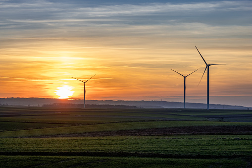 This image depicts a wind farm silhouetted against the backdrop of a setting sun. The towering wind turbines stand as modern sentinels against the colorful hues of the twilight sky, symbolizing the intersection of technology and nature in harnessing renewable energy.