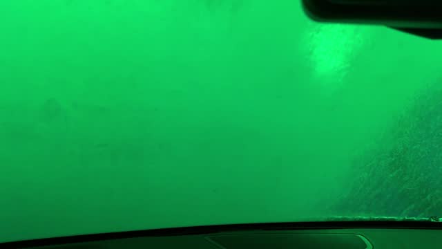A car window is fogged up and the inside of the car is lit up with green lights
