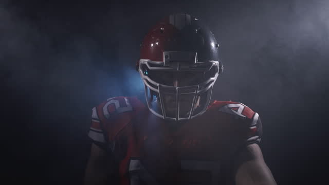 Portrait of determined professional American football player in helmet in dramatic light ready for game. Masculine and agression. Confident man in uniform. Usa team game, extreme sport spirit concept.