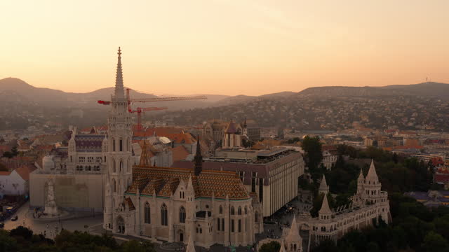 Panoramic view of Buda Castle Hill during sunset. Burning orange sunset skies over the Buda Hills. Cranes indicating the ongoing renovation of Buda Castle. Matthias Church, Fisherman's Bastion Hungary