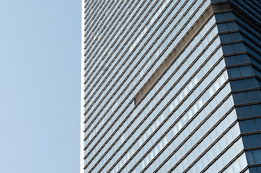 Sleek modern glass and steel office skyscraper jutting into blue sky reflecting fluffy white clouds making a business reflection