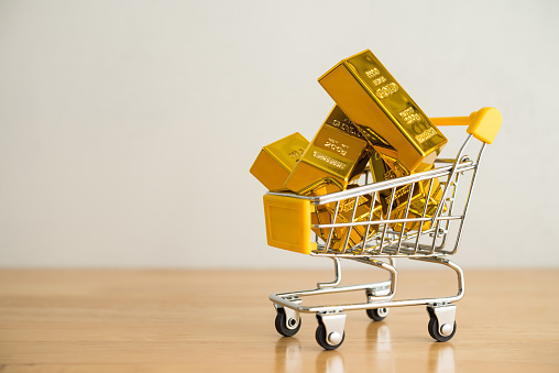Lingotes de oro en carrito de compras sobre mesa de madera con espacio de copia de fondo de pared blanca. photo