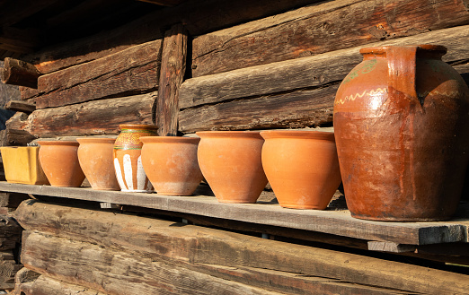 A row of old clay pots on a wooden shelf with selective focus