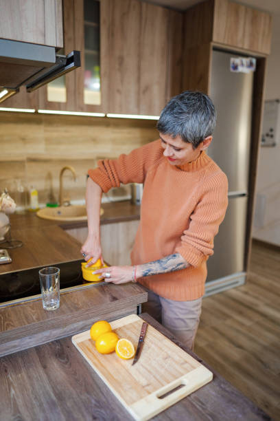 istock Mature woman with tattooed forearm in the kitchen making lemonade 2135282395